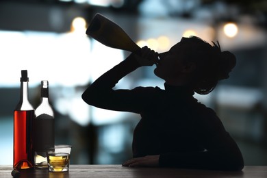 Image of Alcohol addiction. Silhouette of woman drinking sparkling wine from bottle in bar