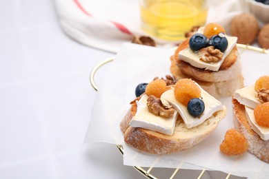 Photo of Tasty sandwiches with brie cheese, fresh berries and walnuts on white tiled table, closeup. Space for text