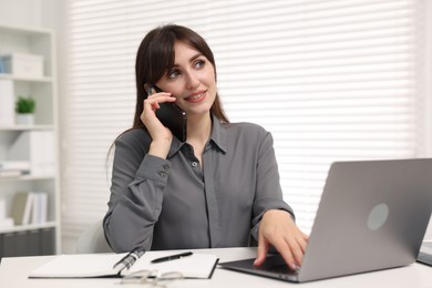 Smiling secretary talking by smartphone at table in office