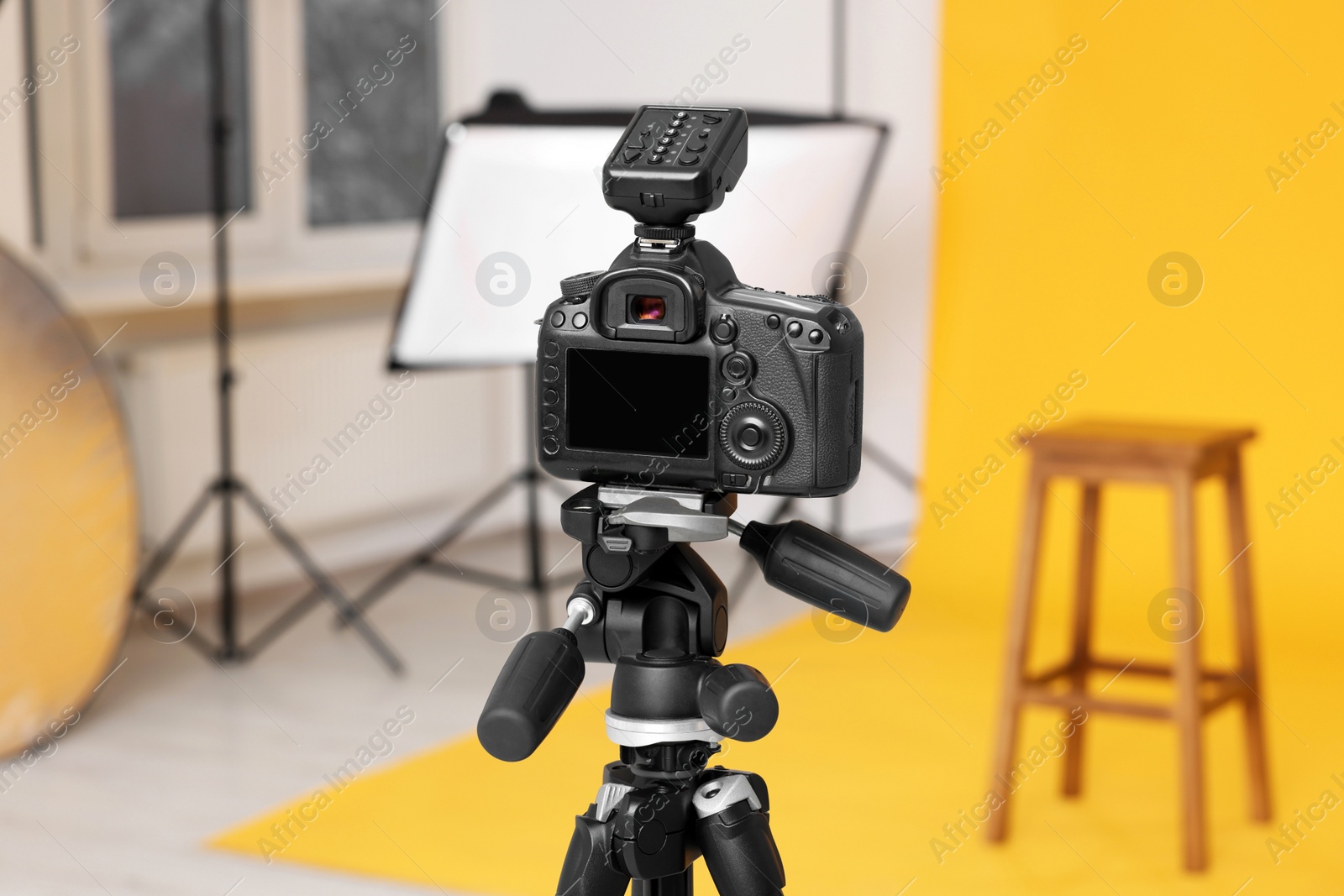 Photo of Camera on tripod, bar stool and professional lighting equipment in modern photo studio