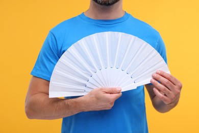 Photo of Man holding hand fan on orange background, closeup