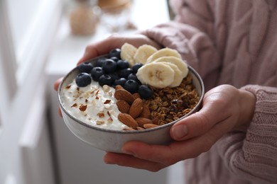 Photo of Woman holding bowl of tasty granola indoors, closeup