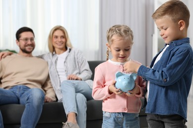 Photo of Family budget. Children putting coin into piggy bank while their parents watching at them indoors, selective focus