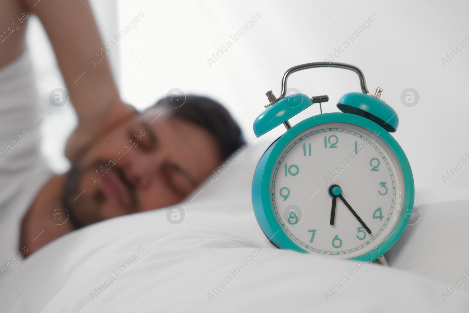 Photo of Sleepy man awaking at home in morning, focus on alarm clock. Space for text