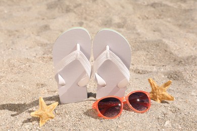 Photo of Stylish flip flops, sunglasses and starfishes on sand