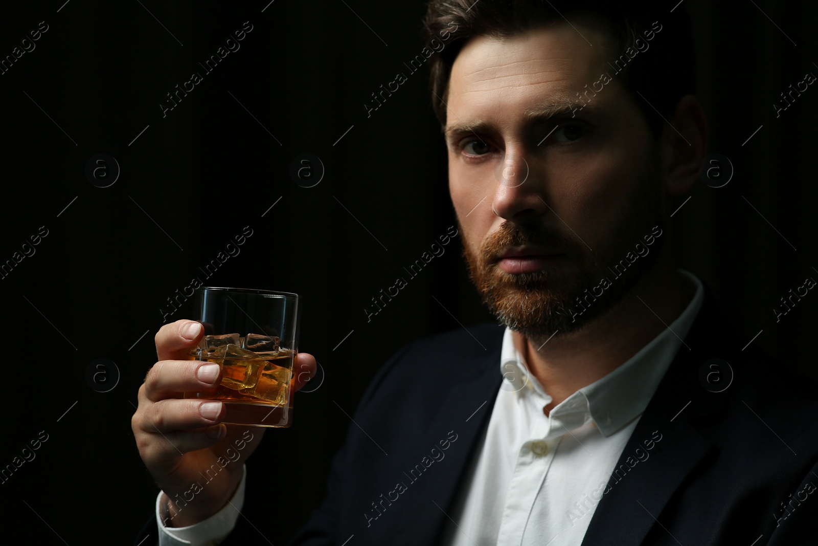 Photo of Handsome man in suit holding glass of whiskey on black background