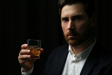 Photo of Handsome man in suit holding glass of whiskey on black background