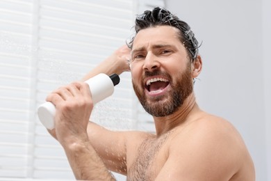 Handsome man with bottle of shampoo singing in shower