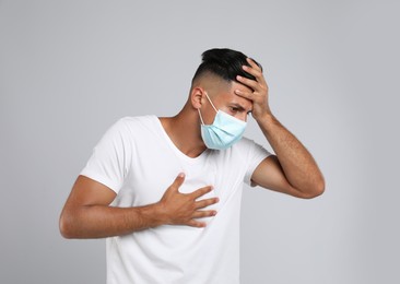 Photo of Man in medical mask suffering from pain during breathing on grey background