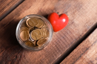 Photo of Red heart and donation jar with coins on wooden table, top view