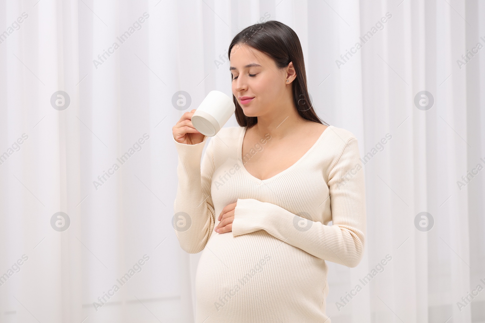 Photo of Beautiful pregnant woman with cup of drink indoors