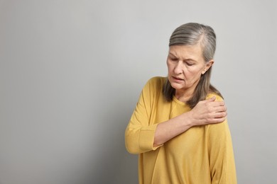 Photo of Arthritis symptoms. Woman suffering from pain in shoulder on gray background, space for text