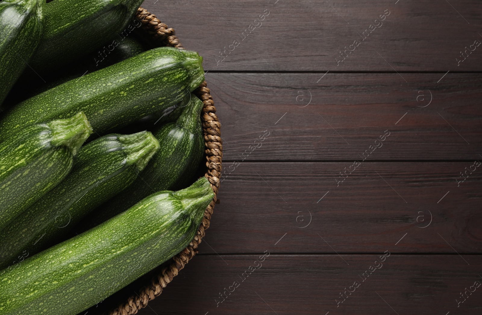 Photo of Raw ripe zucchinis in wicker bowl on wooden table, top view. Space for text