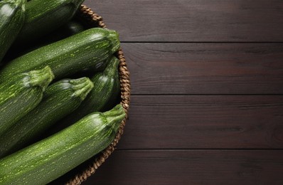 Raw ripe zucchinis in wicker bowl on wooden table, top view. Space for text