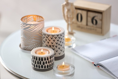 Burning candles in holders and notebook on white table indoors