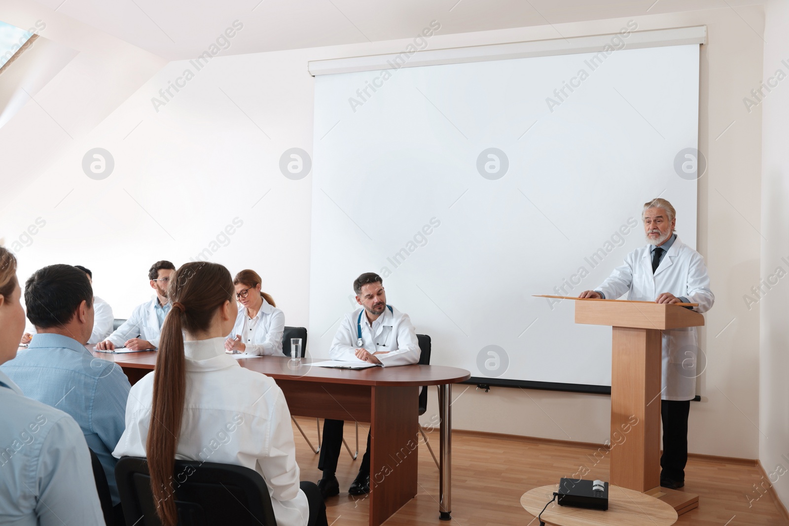 Photo of Senior doctor giving lecture in conference room with projection screen