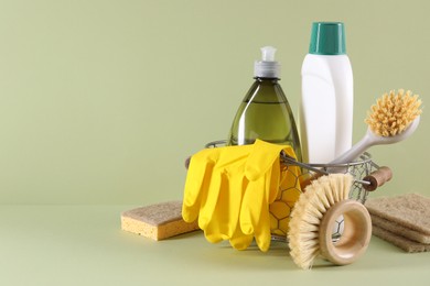 Photo of Set of different cleaning supplies in basket on light green background. Space for text