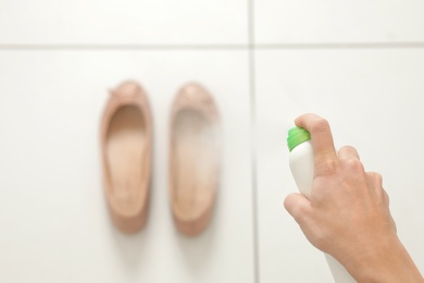 Woman spraying deodorant over pair of shoes at home, closeup. Space for text