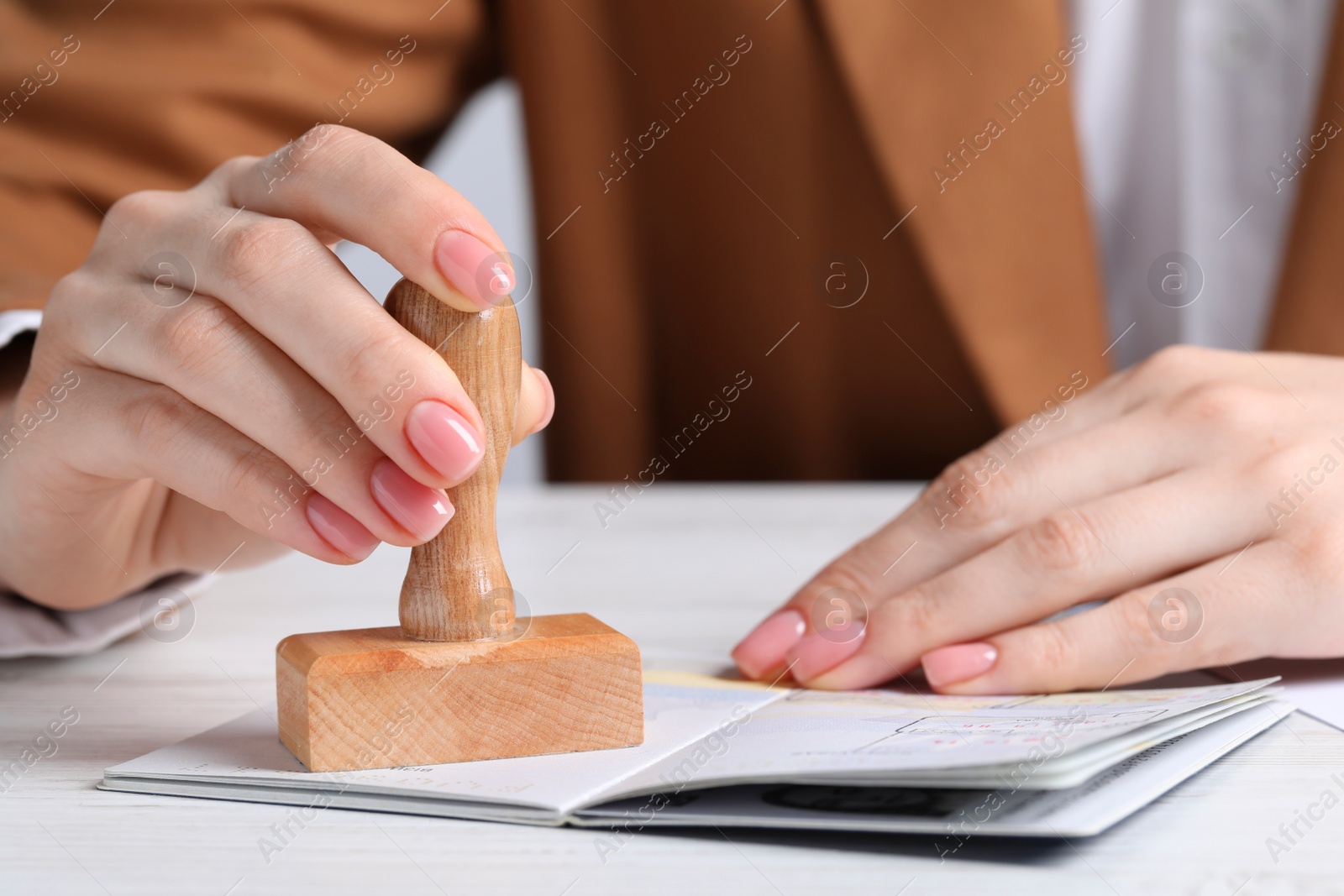 Photo of Ukraine, Lviv - September 6, 2022: Woman stamping visa page in passport at white wooden table, closeup