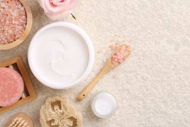 Photo of Flat lay composition with moisturizing cream in open jar and other body care products on light textured table. Space for text