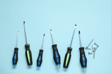 Photo of Set of screwdrivers and screws on light blue background, flat lay. Space for text