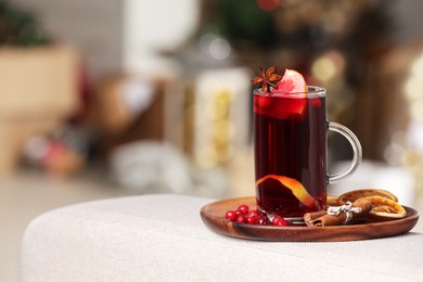 Photo of Aromatic mulled wine in cup and ingredients on sofa armrest against blurred background. Space for text