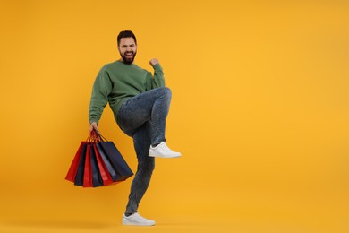 Photo of Excited man with many paper shopping bags on orange background. Space for text