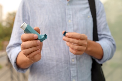 Photo of Man using asthma inhaler outdoors, closeup. Health care