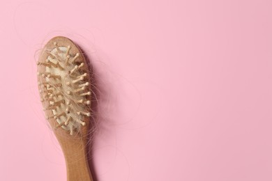 Photo of Wooden brush with lost hair on pink background, top view. Space for text