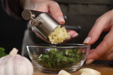 Photo of Woman squeezing garlic with press at table, closeup