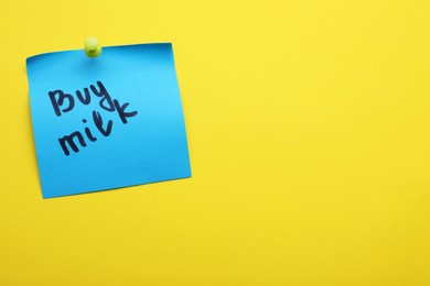 Photo of Paper note with words Buy milk pinned on yellow background, space for text