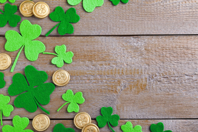 Photo of Flat lay composition with clover leaves and gold coins on wooden table, space for text. St. Patrick's Day celebration