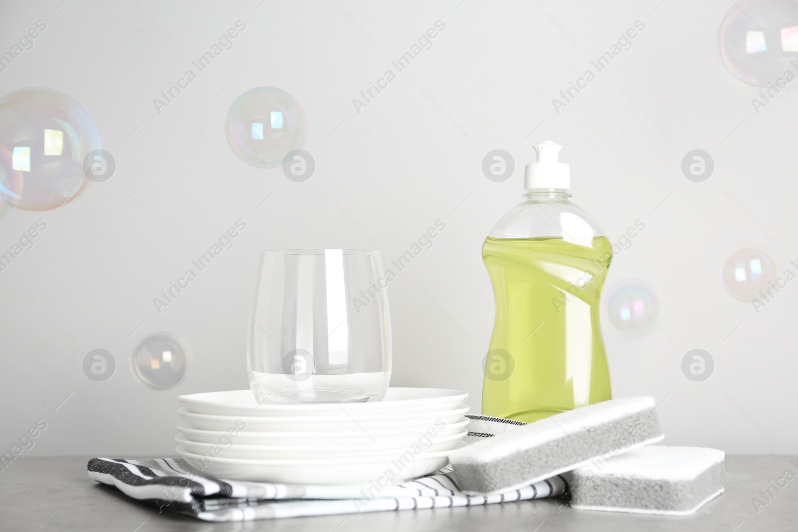 Photo of Cleaning supplies for dish washing, plates and soap bubbles on grey background