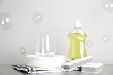 Cleaning supplies for dish washing, plates and soap bubbles on grey background