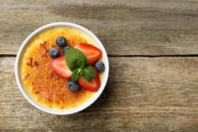 Photo of Delicious creme brulee with berries and mint in bowl on wooden table, top view. Space for text