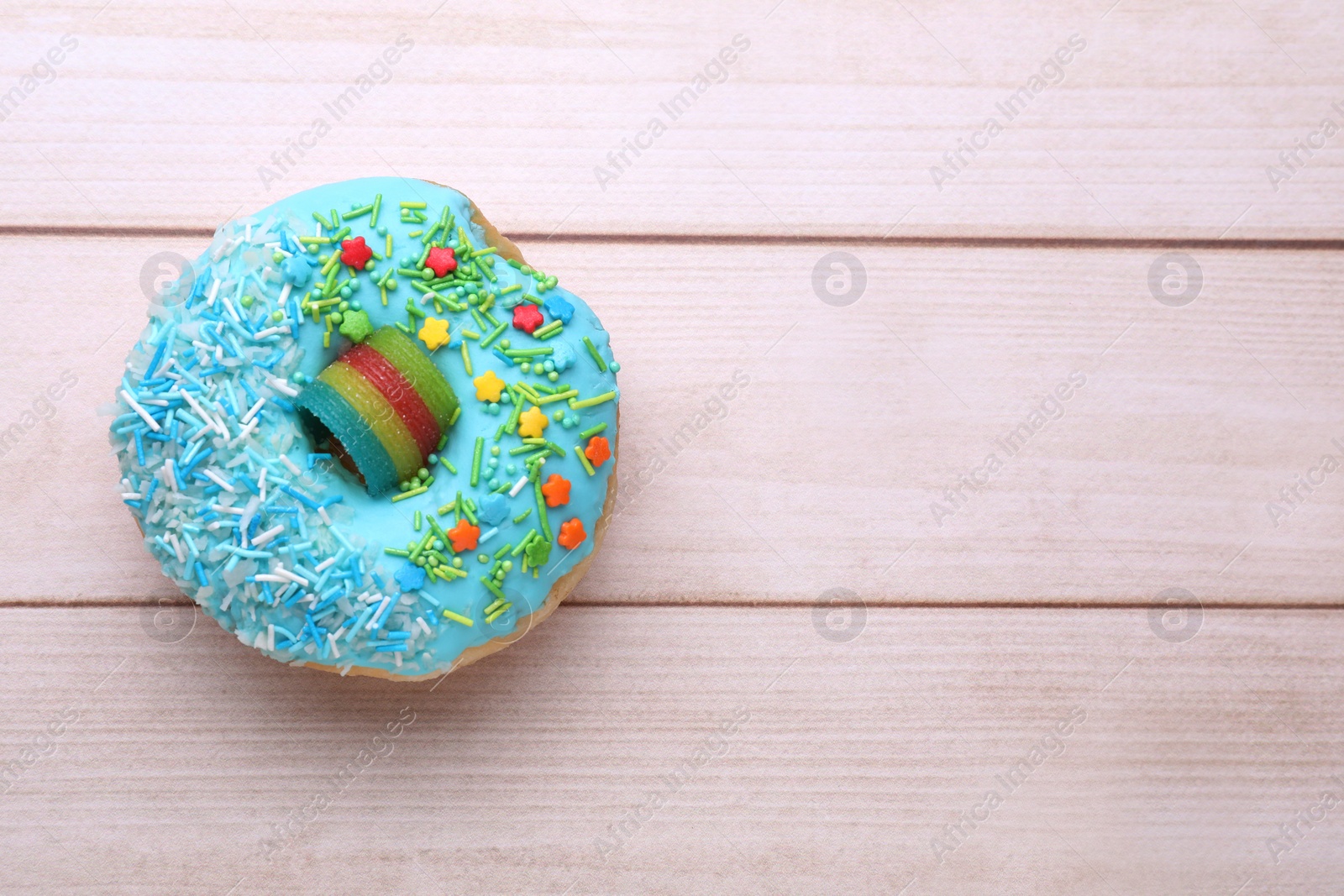 Photo of Glazed donut decorated with sprinkles on white wooden table, top view. Space for text. Tasty confectionery