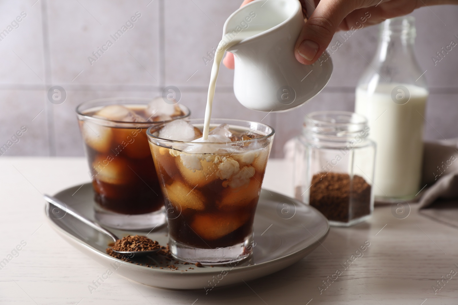 Photo of Woman pouring milk into glass with refreshing iced coffee at light table, closeup