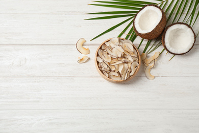 Photo of Tasty coconut chips on white wooden table, flat lay. Space for text