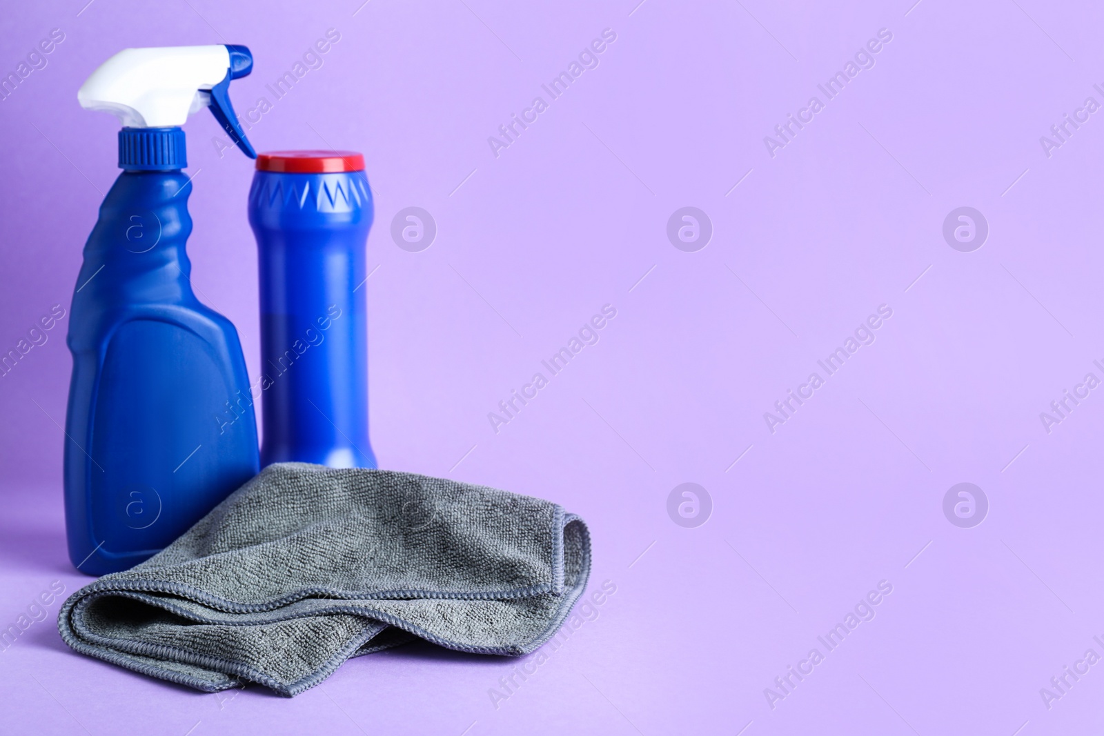 Photo of Grey microfiber cloth and detergents on light background, space for text