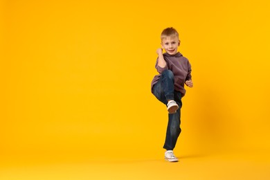 Photo of Happy little boy dancing on yellow background. Space for text