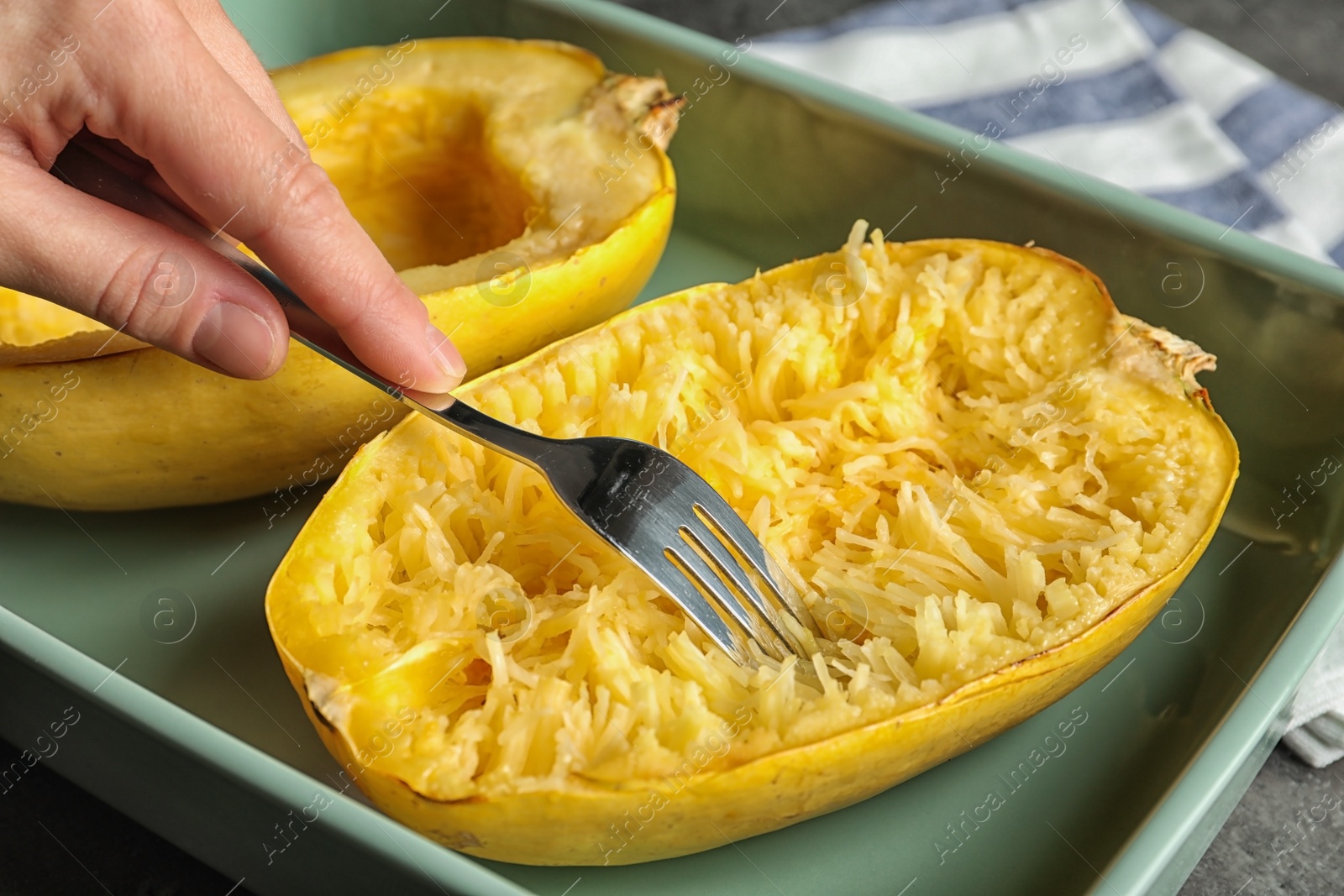 Photo of Woman scraping flesh of cooked spaghetti squash with fork on table, closeup