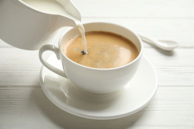 Photo of Pouring milk into cup of hot coffee on white wooden table