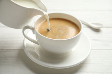 Pouring milk into cup of hot coffee on white wooden table