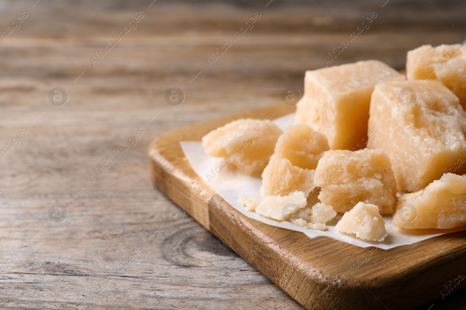 Photo of Pieces of delicious parmesan cheese on wooden table, closeup. Space for text