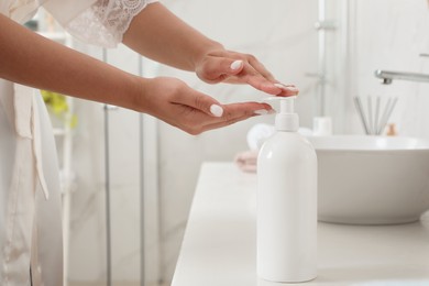 Photo of Beautiful young woman using washing gel in bathroom, closeup. Skin care cosmetic