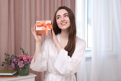 Photo of Beautiful happy young woman holding gift box in room