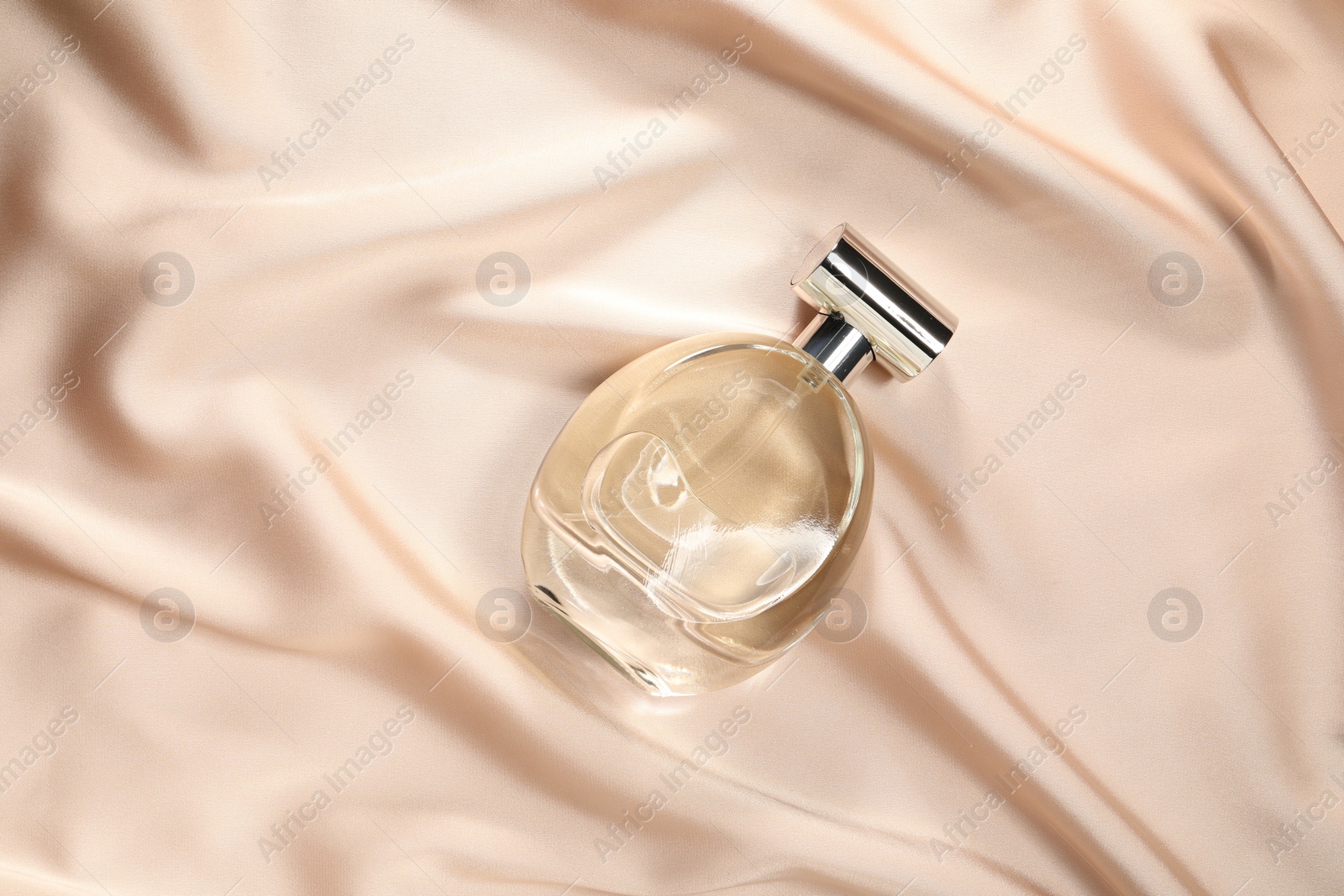 Photo of Luxury perfume in bottle on beige silk fabric, top view