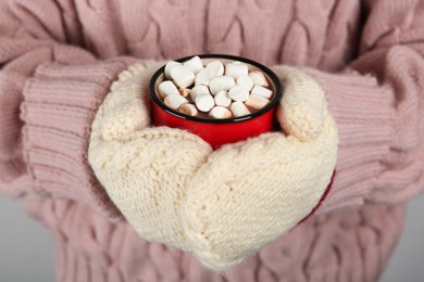 Photo of Woman in knitted mittens holding cup of delicious hot chocolate with marshmallows, closeup
