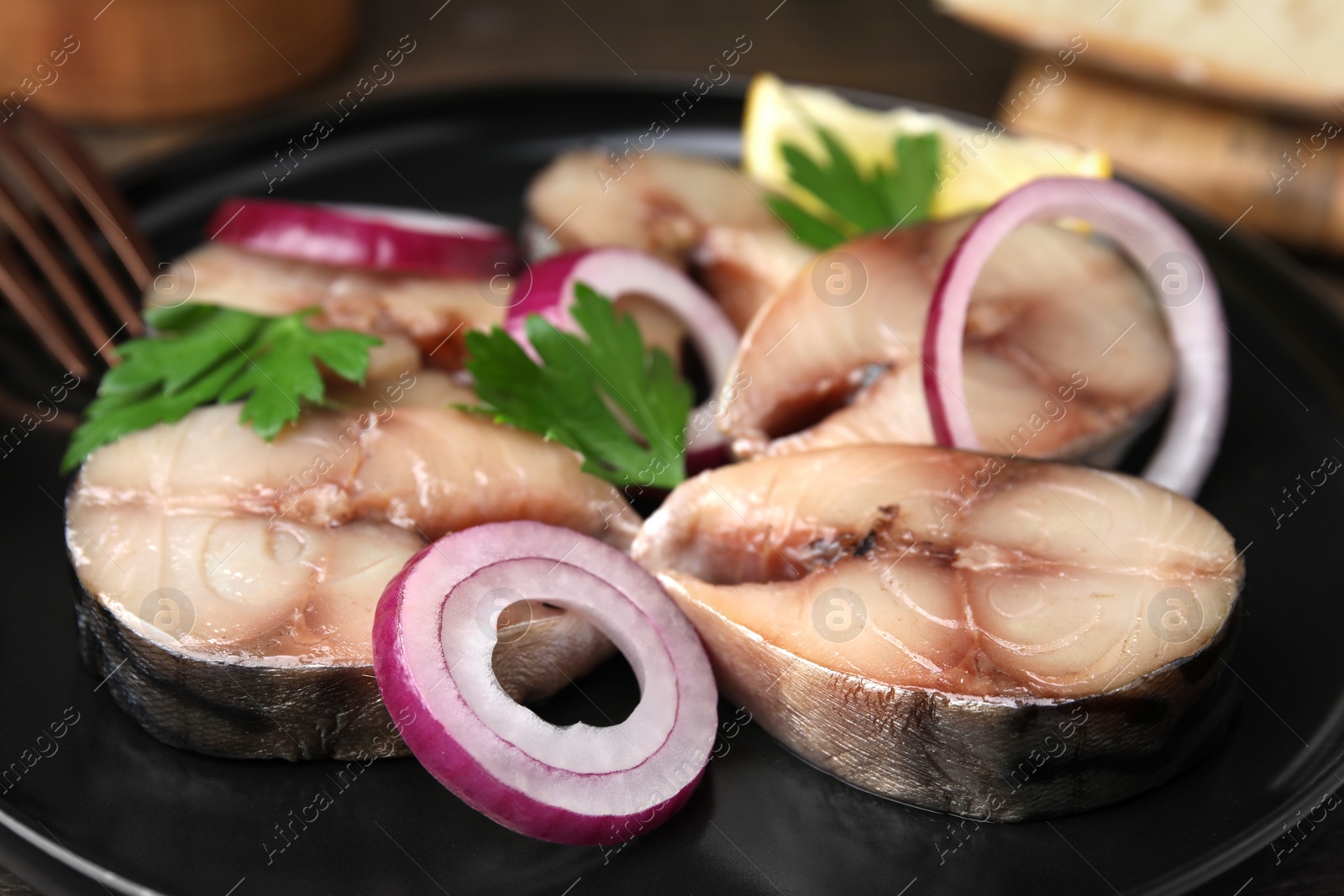 Photo of Slices of tasty salted mackerel, onion rings and parsley on black plate, closeup