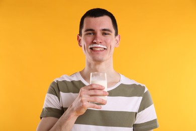 Photo of Happy man with milk mustache holding glass of tasty dairy drink on orange background